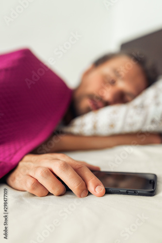 Sleeping young handsome man while holding his mobile phone. Screen on the phone is turned off