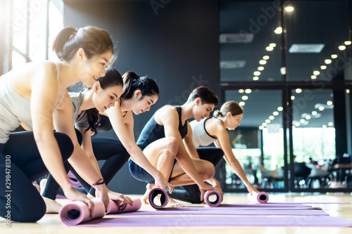 Group of sporty diversity people rolling the yoga mat after training yoga workout in studio room at gym or fitness club. They have a good body shape and fit due to exercise and training yoga.