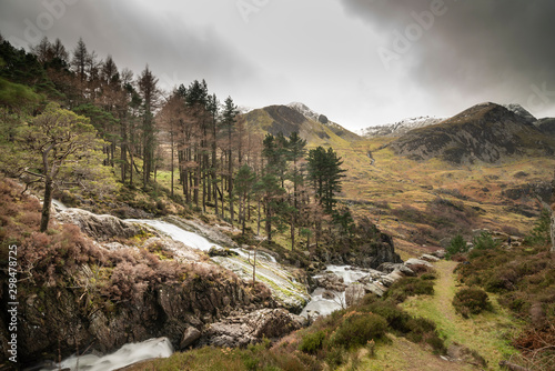 Stunning landscape image of Ogwen Valley river and waterfalls during Winter with snowcapped mountains in background photo