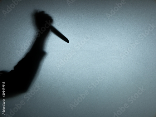 Halloween concept. Blurred shadow of hand holding sharp knife behind white mirror background. Murder scene.