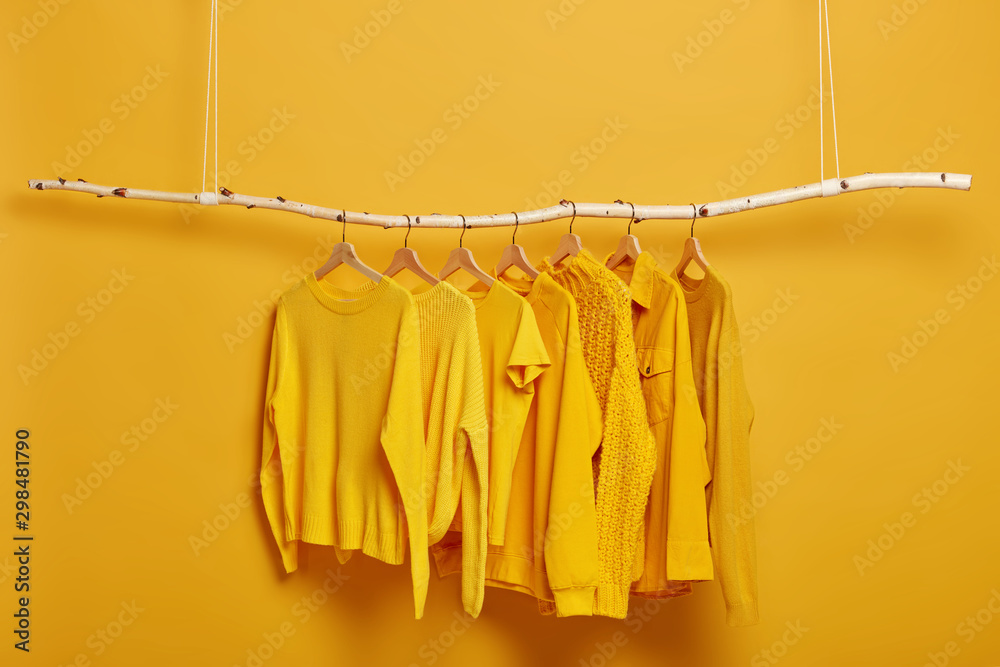 Collection of plain yellow sweaters and jackets for women hanging on rack in dressing room. Selective focus. Fashionable winter or autumn clothes. Sale in fashion store. Dressing closet with clothing - obrazy, fototapety, plakaty 
