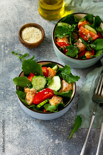 Tasty and healthy Salmon Grilled Salad with cucumber, tomatoes, fresh arugula and sesame seeds on a gray stone table. Free space for your text.
