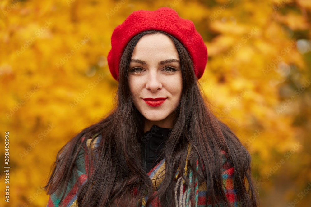 Facial portrait of beautiful Caucasian woman warmly clothed, posing in autumn outdoor, looking directly at camera with calm facial expression, lady dresses stylish red beret, spending time in open air Facial portrait of beautiful Caucasian woman warmly clothed, posing in autumn outdoor, looking directly at camera with calm facial expression, lady dresses stylish red beret, spending time in open air