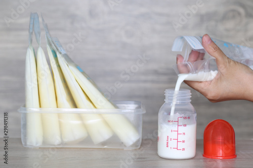 woman pouring milk in to bottles for new baby on wooden table
