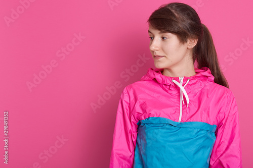 Portrait of attractive sporty woman in sportive shirt, charming lady having pony tail, looking aside, isolated over pionk studio background. Copy space for your advertismeent or promotion text. photo