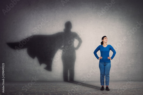 Tela Brave woman keeps arms on hips, smiling confident, casting a superhero with cape shadow on the wall
