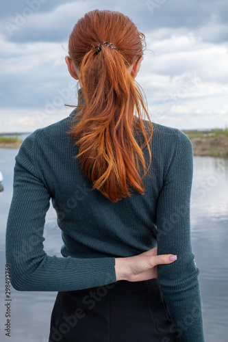 a red haired girl in a green turtleneck stands with her back half turned