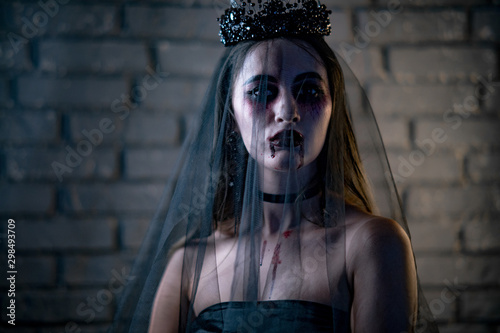 Obraz na płótnie Woman in a carnival costume of a vampire bride stands in black wedding dress, veil and diadem