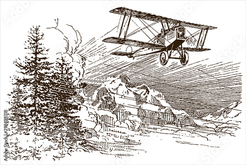 Vintage biplane aircraft flying over snowy mountaineous region with trees