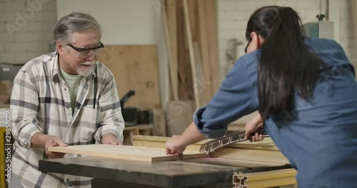 Asian senior carpenter and teen female capenter using circular saw for cutting wooden plank together in carpentry workshop. photo