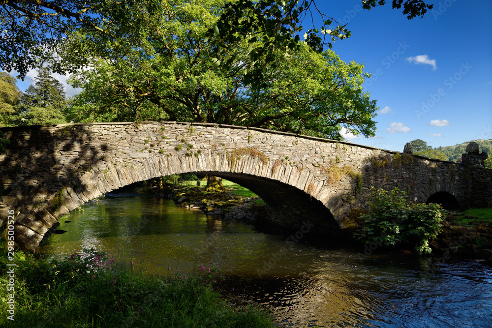 Stone arch Pelter Bridge in evening sun over the River Rothay at Rydal Cumbria Lake District National Park England
