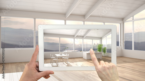 Augmented reality concept. Hand holding tablet with AR application used to simulate furniture and design products in empty interior with parquet, kitchen with island and dining table