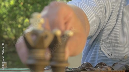 Old man prepares the chess game outside in the garden at the table and puts the black figures side by side.