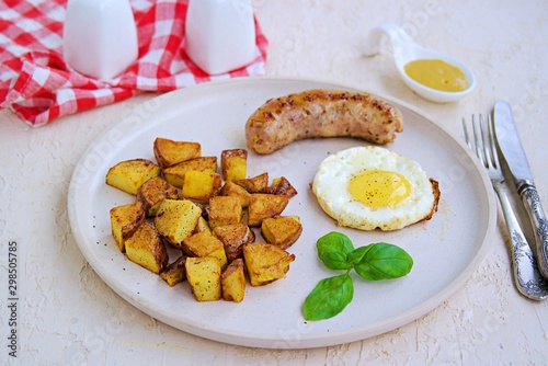 Large breakfast, home fries potatoes, pork sausage and fried egg on a white clay plate on a light concrete background. American food