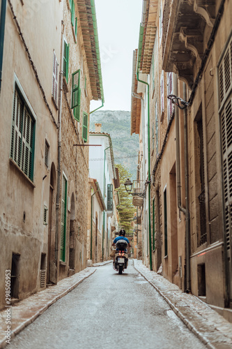Man riding a motorcycle in an alley surrounded by old houses in the picturesque town of Soller  Mallorca  Spain. Vertical photo.