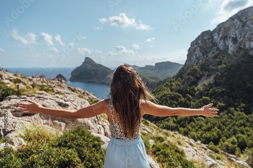 Epic shot of a woman with arms open on the edge of a rock contemplating the incredible view of Cape Formentor in Majorca, Balearic Islands, Spain. Vertical photo. photo