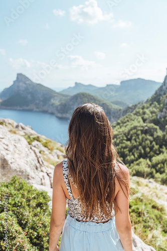Epic shot of a woman hiking on the edge of a rock contemplating the incredible view of Cape Formentor in Majorca, Balearic Islands, Spain. Vertical photo.