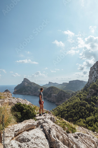 Epic shot of a man hiking on the edge of a rock contemplating the incredible view of Cape Formentor in Majorca, Balearic Islands, Spain. Vertical photo.