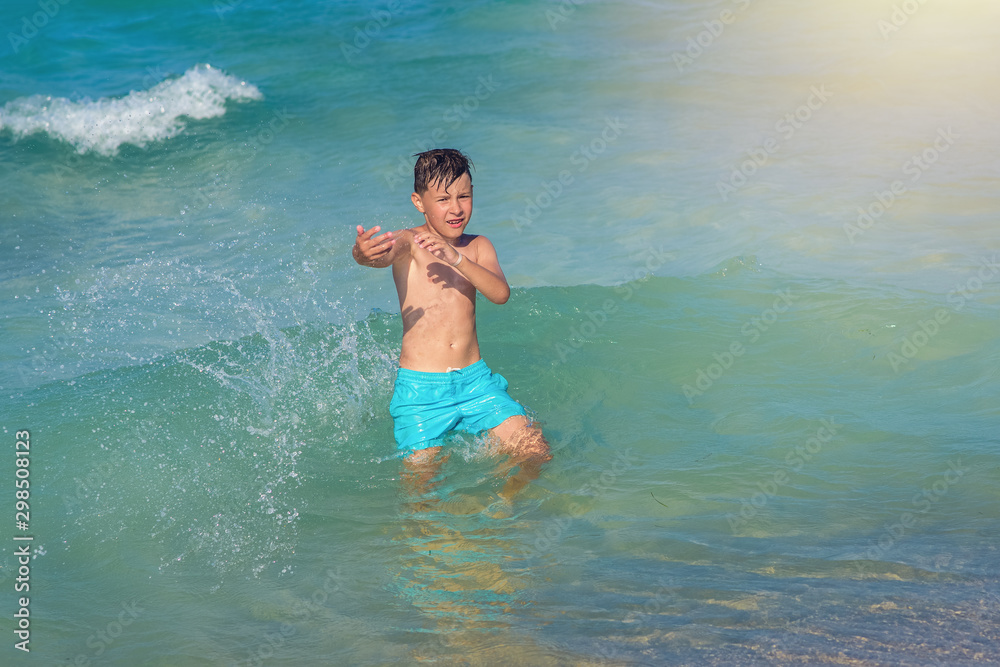 Cute European boy in blue swimming shorts playing in  clear blue ocean water.  He is enjoying his summer holidays.