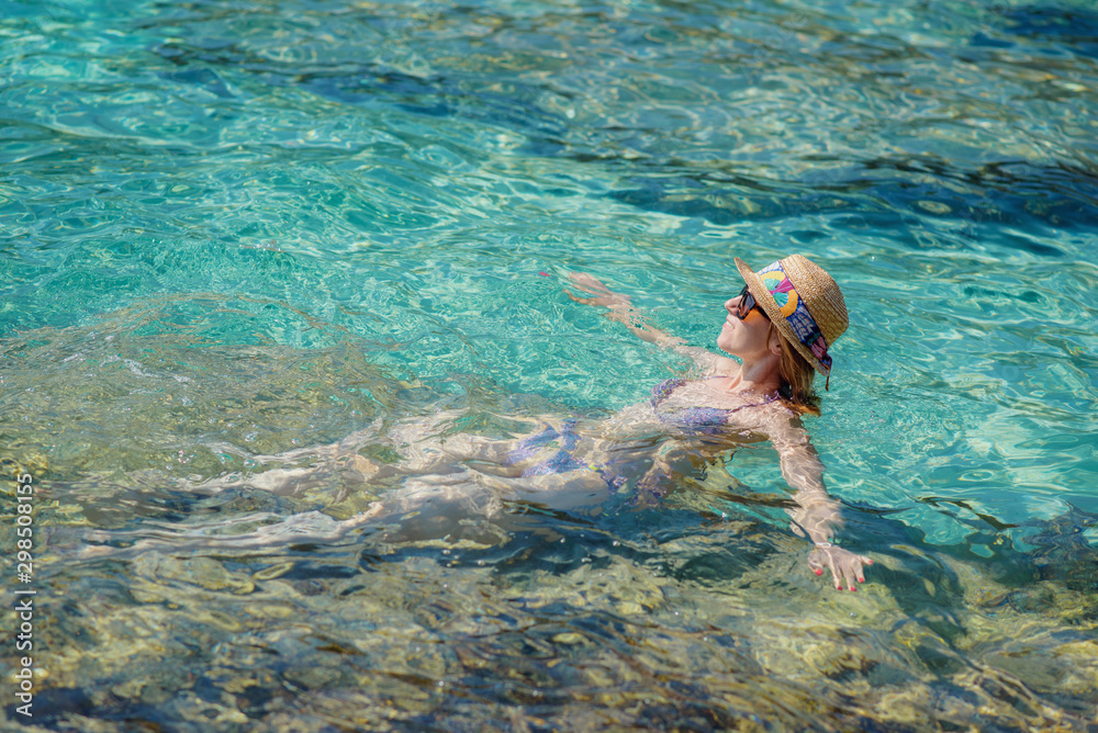 Slender European girl in sun hat swimming in ocean during vacations. She relaxing and enjoying her  summer rest.