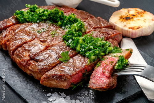 Ready to eat black Angus beef rib eye steak sliced with herbs, garlic and sauce on slate Board. Ready meal for dinner on black wooden background