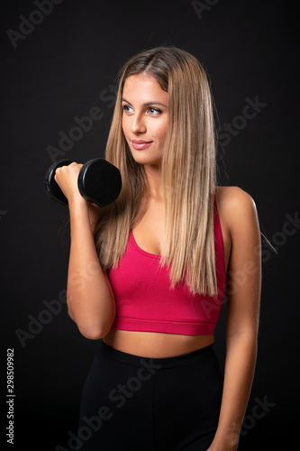 Young sport blonde woman making weightlifting over isolated black background