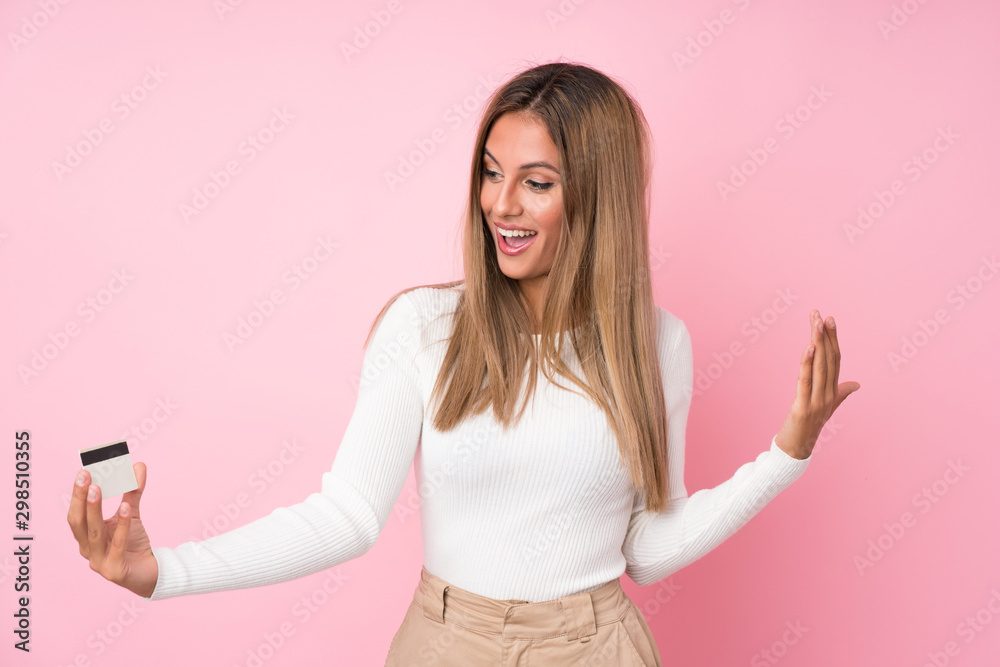 Young blonde woman over isolated pink background holding a credit card