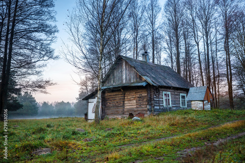 Wooden log cabin abandoned in the autumn forest at dawn.