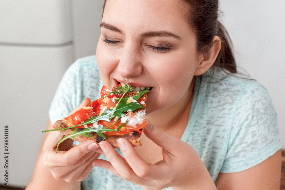 Binge Eating. Chubby girl sitting at kitchen table eating pizza closed eyes delightful close-up Binge Eating. Chubby girl sitting at kitchen table eating pizza closed eyes delightful close-up