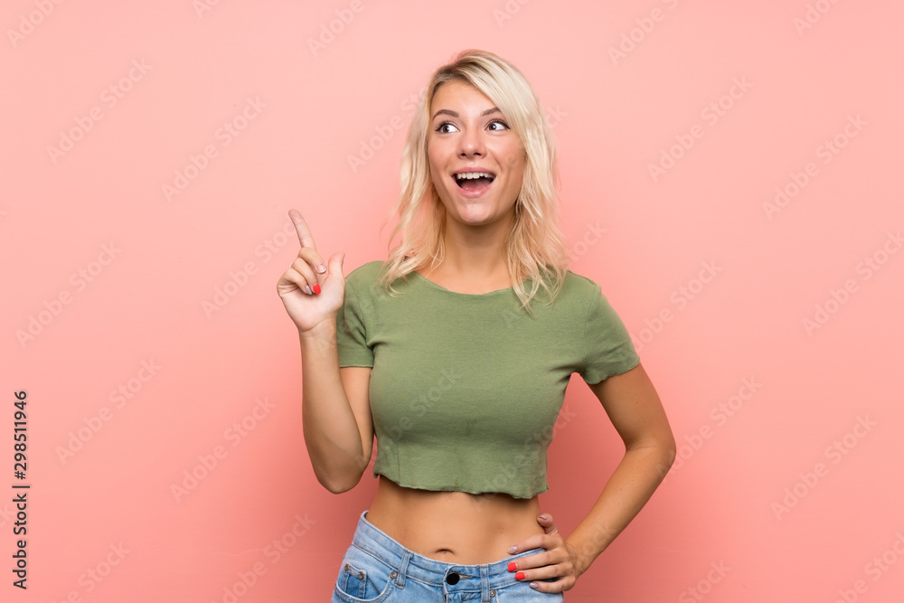 Young blonde woman over isolated pink background pointing up and surprised