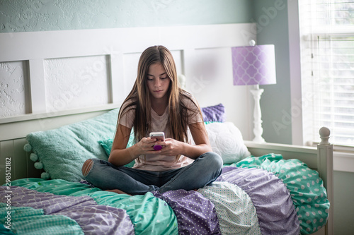 Принти на полотні Adolescent teen girl texting on a smartphone sitting in bed at home in her bedro