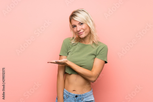Young blonde woman over isolated pink background presenting an idea while looking smiling towards
