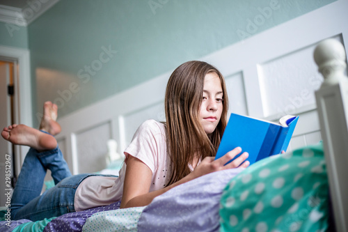 Adolescent teen girl reading a book while lying in bed at home in her bedroom. Lifestyle photo photo