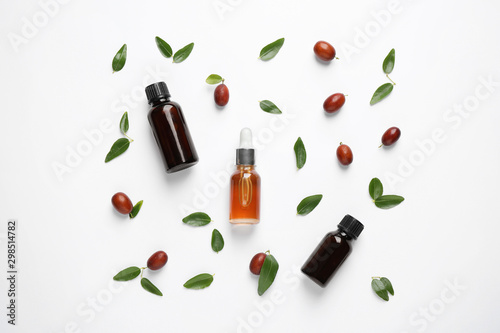 Glass bottles with jojoba oil and seeds on white background, top view