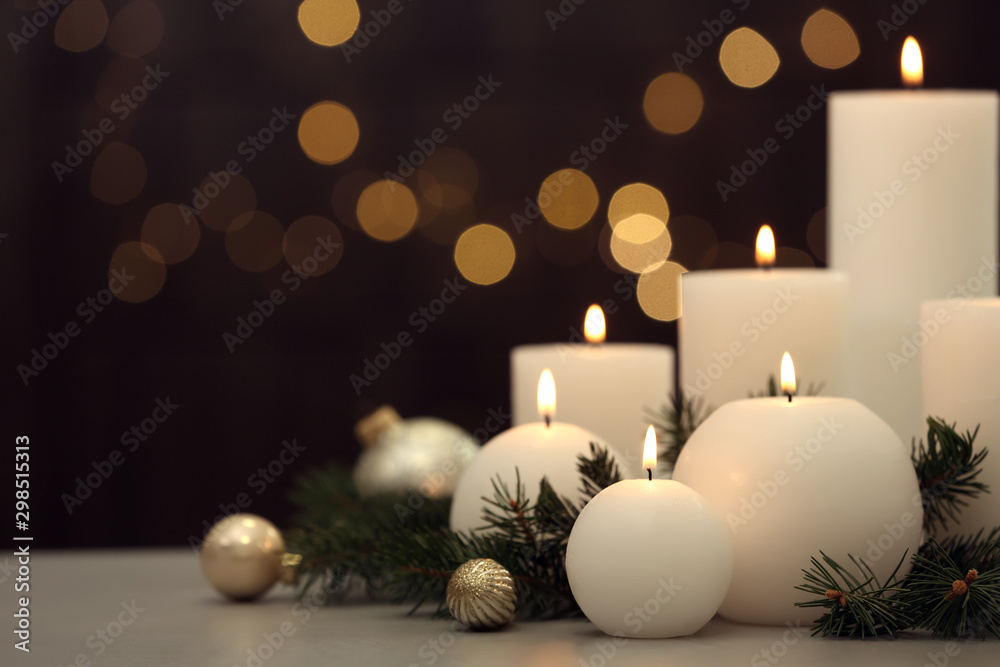 Burning white candles with Christmas decor on table against blurred lights. Space for text