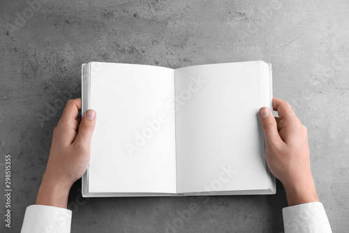 Man holding blank book at grey table, top view. Mock up for design