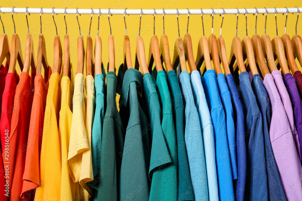 Rack with bright clothes on yellow background. Rainbow colors Rack with bright clothes on yellow background. Rainbow colors