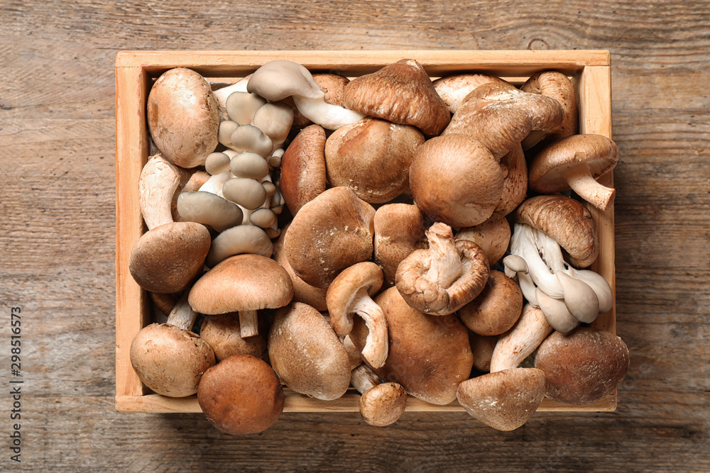 Different wild mushrooms in crate on wooden background, top view