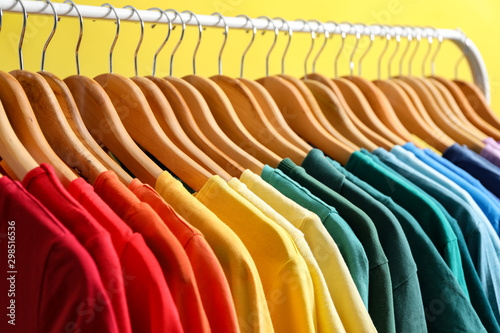 Rack with bright clothes on yellow background. Rainbow colors