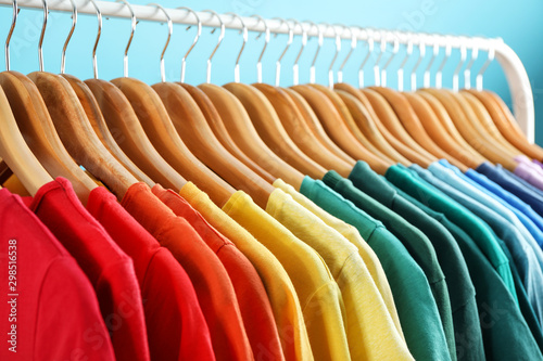 Rack with bright clothes on blue background. Rainbow colors