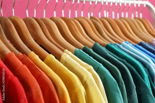 Rack with bright clothes on pink background. Rainbow colors