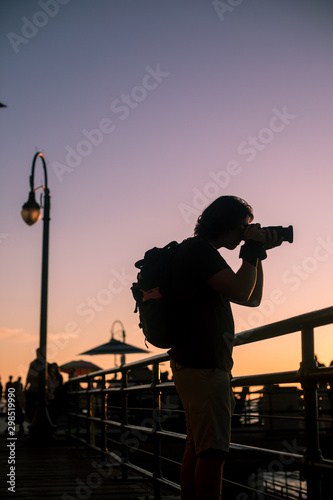 A young male photographer photographs the sunset from the Santa Monica Pier.