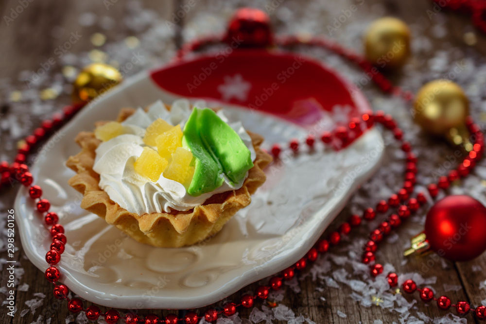 Tasty cake with cream and candied fruit in a New Year's plate for the holiday table ext to decorations Tasty cake with cream and candied fruit in a New Year's plate for the holiday table ext to decorations