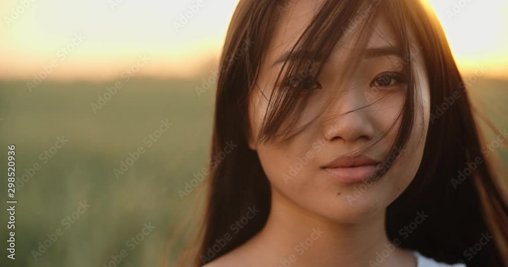 Cute asian girl standing in the wheat field during sunset as the wind blows her hair, looking at camera - close up portrait shot 4k footage Cute asian girl standing in the wheat field during sunset as the wind blows her hair, looking at camera - close up portrait shot 4k footage