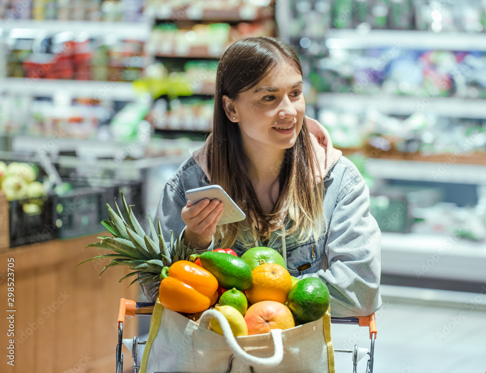 A young woman buys groceries in a supermarket with a phone in her hands. A young woman buys groceries in a supermarket with a phone in her hands.