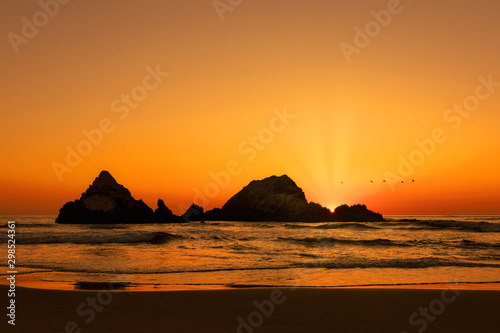 Sun rising over rock formations as pelicans fly over  waves