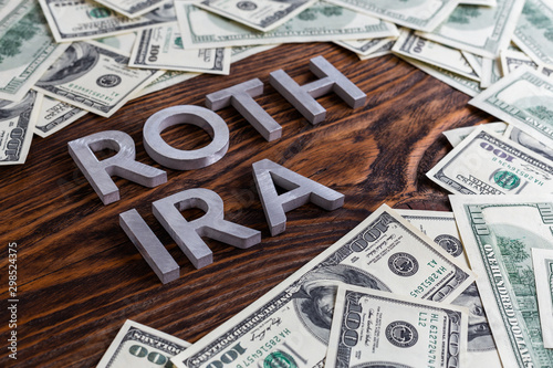 words ROTH IRA laid on wooden surface by metal letters with us dollar banknotes photo