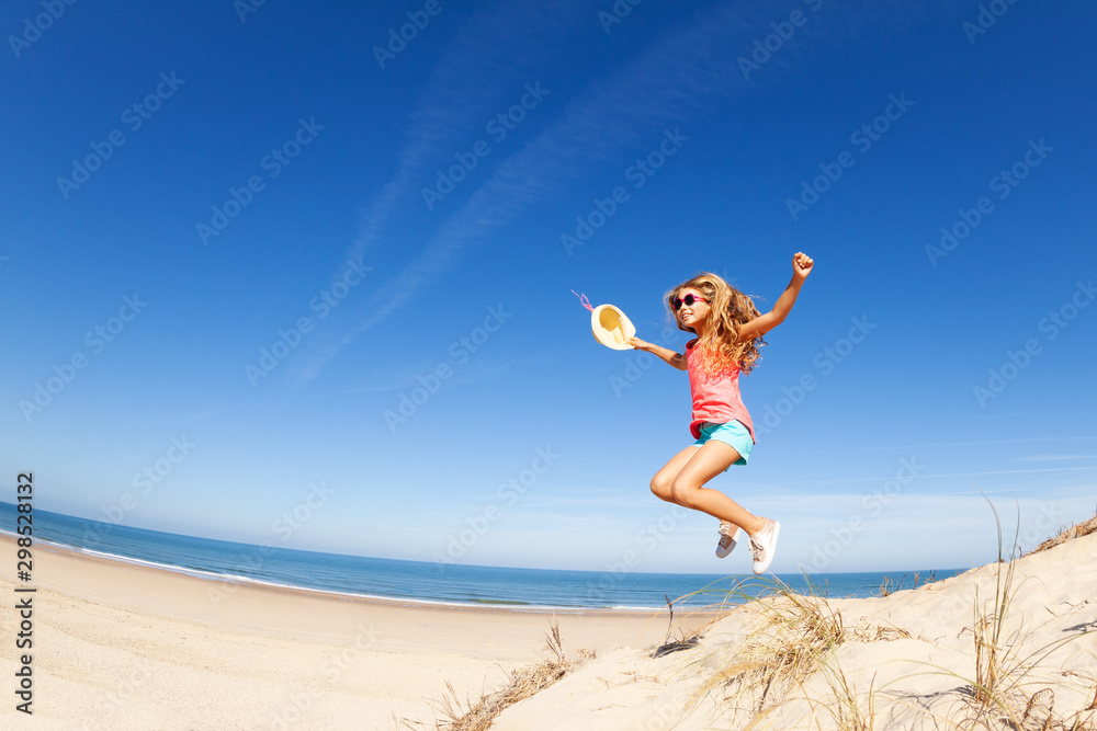 Obraz premium Happy little beautiful girl jump from sand dune