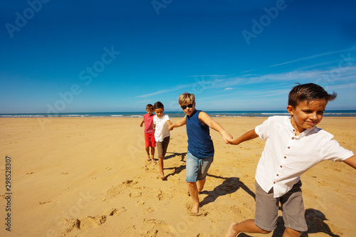Group of kids run, hold hands together on a beach