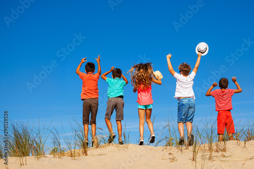 View from behind of a kids group jump on sand dune
